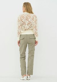 Krém színű, virágos csipkemintás kötött pulóver, olívazöld cargo nadrággal párosítva; a fehér magas sarkú cipő egészíti ki a szettet.