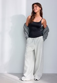 Débardeur noir, pull gris oversize, et pantalon de survêtement gris clair à jambes larges. Le tissu semble doux, avec une coupe décontractée sur l'ensemble.