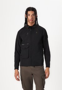 Black lightweight jacket with a high collar, zip closure, and a front patch pocket. Made of soft, smooth material; features elastic cuffs.