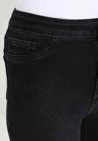 Svarta jeanse med slim fit, med en enda bakficka och subtila sömnadsdetaljer. Slät textur och minimal design.