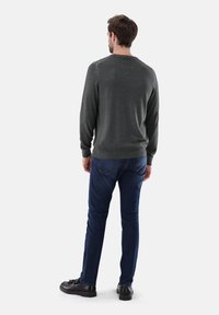 Dunkelgrauer, langärmeliger Pullover mit gerippten Bündchen, kombiniert mit blauen Jeans und schwarzen Schuhen. Der Pullover hat eine glatte Textur und ein einfaches Design.