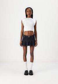 Top corto blanco con textura acanalada y detalles de volantes en los hombros, combinado con una falda corta de mezclilla oscura acampanada y zapatos negros, complementado con calcetas blancas.