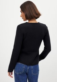 Must mustriga kampsun pikka varrukatega, ümmarguse kaelusega ja tekstureeritud viimistlusega. Sellel on sirge lõige ja see on paaritatud siniste kõrge vöökohtadega teksadega.