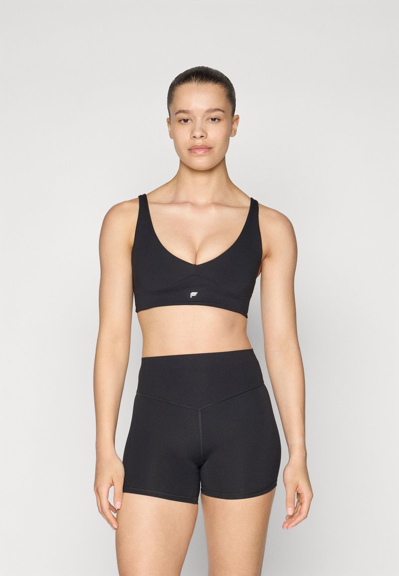 Sujetador deportivo negro con un diseño de escote en V, tirantes anchos y un pequeño logo; combinado con shorts negros de tiro alto, ambos en tejido suave.