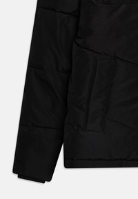 Chaquetón negro tipo puffer con textura acolchada, que cuenta con un bolsillo oculto. Los puños son elásticos, lo que mejora la calidez y el ajuste.