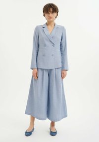 Lichtblauwe, dubbelgeknoopte blazer met gesneden revers en twee knopen, gecombineerd met wijde broekspijpen in een bijpassend materiaal en kleur.