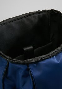 Otwarty niebiesko-czarny plecak z widoczną, wyściełaną komorą wewnętrzną oraz pętlą na pasek do noszenia.