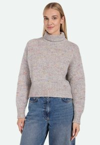 Light gray, chunky knit turtleneck sweater featuring multicolored flecks, ribbed cuffs, and waistband, paired with blue denim jeans.