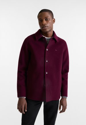 Giacca in misto lana color bordeaux con colletto, bottoni frontali e tasche laterali; presenta una texture liscia e una vestibilità sartoriale.