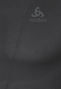 Tissu noir avec une texture à pois subtile comportant un logo gris Odlo. Le matériau est léger et respirant, adapté aux vêtements de sport.