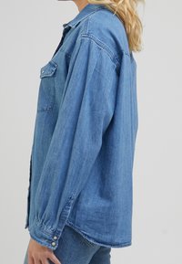 Hellblaues Denimhemd mit Kragen, einer Brusttasche, Knopfverschluss und langen Ärmeln mit knöpfbaren Manschetten.