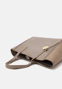Beige nubuck tote bag med sidelægningsdetalje, glat tekstur, to flade hanke og en lukning i guldhardware.