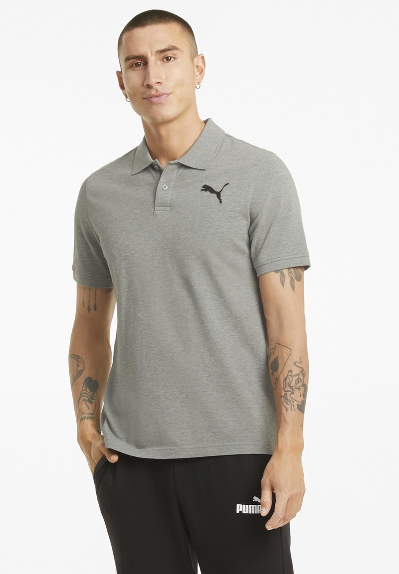 Graues Polohemd mit schwarzem Puma-Logo, kurzen Ärmeln und klassischem Kragen. Getragen mit schwarzen Hosen, die eine glatte Stofftextur zeigen.