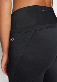 Leggings neri a vita alta con una texture liscia, cintura ampia e una tasca con zip discreta sulla parte posteriore. Dettaglio del logo in bianco.