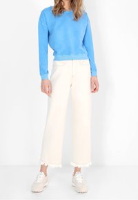 Felpa blu, pantaloni a gamba larga crema con orlo sfrangiato e sneakers chiare. Tessuto morbido, vestibilità comoda, linee pulite, design semplice.