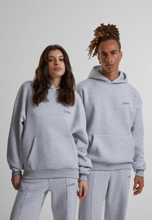 Grå bomullshoodies med frontlommer og ribbestrikkede mansjetter, med en liten logo på brystet. Matchende grå joggebukser vises.