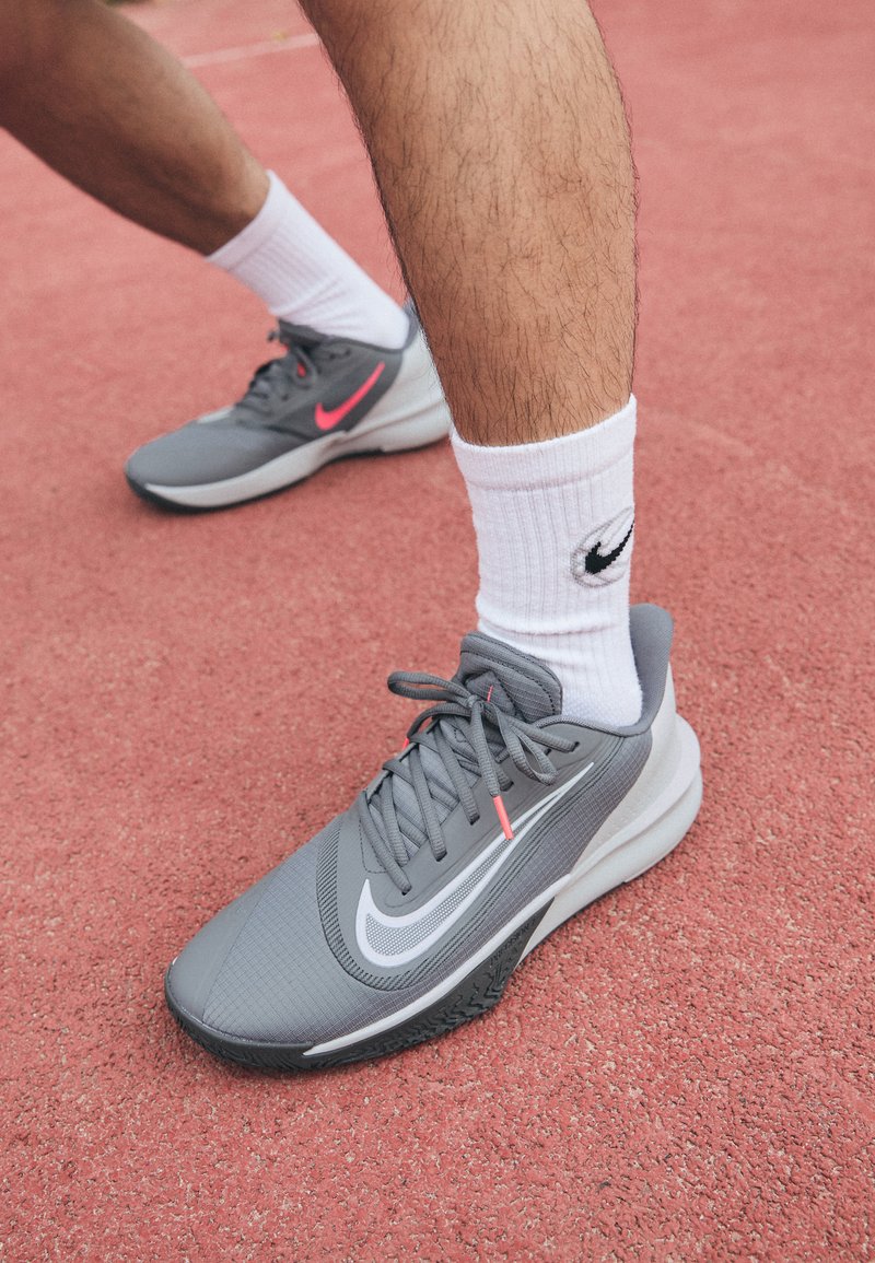 Des chaussures de sport grises avec une tige en maille, un logo swoosh blanc et une semelle en caoutchouc noir texturé. Associées à des chaussettes blanches arrivant aux mollets.