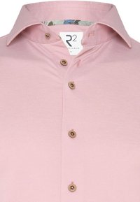 Lichtroze shirt met een gestructureerd patroon. Beschikt over een gespreide kraag, bruine knopen en een kleurrijke accent aan de binnenkant van de kraag. Maatlabel: M.