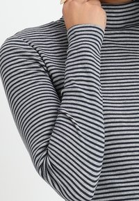 Långärmad polotröja i grå och marinblå randig ribbad tyg. Har en åtsittande form och texturerad yta.