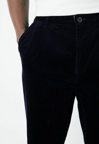 Navy corduroy pants with vertical ribbed texture, side pockets, and a single button closure at the waist.