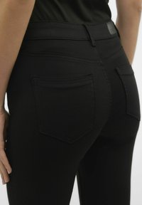 Mustad denim teksad, mis on kitsas sobivus, kahe tagatasku ja siledat tekstuuri ning kontrastrõivaste tikkimisega õmbluste ääres.