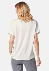 Witte T-shirt met korte mouwen en een losse fit, met een gladde textuur. Draagt met zwart-wit geblokte broeken, vanuit de achterkant bekeken.