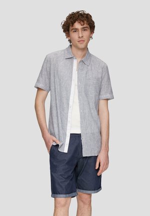 Kurzarm, hellblau gesprenkeltes Hemd mit Knopfleiste und Tasche in Weiß, kombiniert mit dunkelblauen, hochgekrempelten Denim-Shorts.