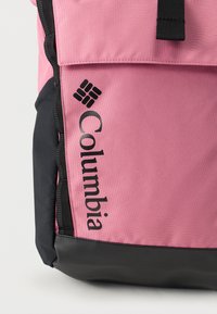 Ροζ υφασμάτινο σακίδιο Columbia με μαύρη βάση, με κλείσιμο με καπάκι και το λογότυπο της μάρκας τυπωμένο μαύρο στο μπροστινό μέρος.