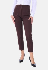 Pantaloni marroni a vita alta con una vestibilità sartoriale, caratterizzati da pieghe verticali e una texture liscia. Abbinati a décolleté nere a punta.