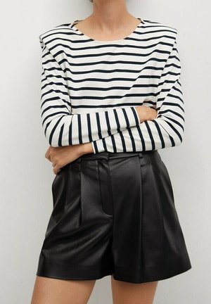 Haut à manches longues rayé en blanc et bleu marine, avec des accents aux épaules, associé à un short en cuir noir taille haute avec des plis.