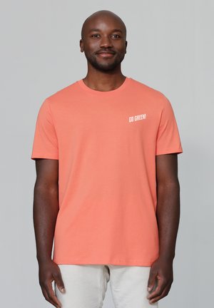 Korallenfarbiges Baumwoll-T-Shirt mit kurzen Ärmeln, Rundhalsausschnitt und "GO GREEN!" in Weiß auf der linken Brustseite bedruckt. Glatte Textur.