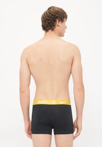 Crne bokserice s žutim Nike pojasom, elastičnog materijala, prilagođenog dizajna i glatke teksture, prikazane sa stražnje strane.