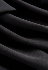 Tessuto nero con una superficie liscia e strutturata, caratterizzato da molteplici pieghe che ne evidenziano la caduta e la morbidezza.