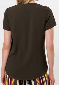 Haut noir olive à manches courtes avec un col rond, présentant un ourlet courbé et une texture lisse, associé à un pantalon multicolore à rayures.