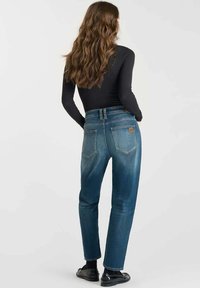 Jeans de mezclilla azul con cintura alta, pierna recta y un lavado desgastado. Presentan bolsillos traseros y una etiqueta de logo en la parte trasera derecha.