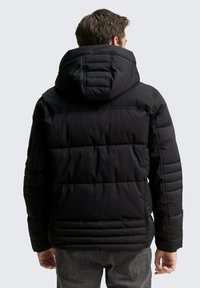 Černá prošívaná bunda s kapucí, obsahující prošívané detaily, hladkou texturu a elastické manžety. Zadní pohled ukazuje strukturovanou siluetu.