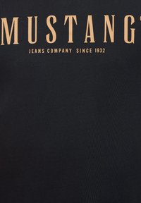 Czarny bawełniany t-shirt z dużym beżowym napisem „MUSTANG” oraz „JEANS COMPANY SINCE 1932” umieszczonym na środku klatki piersiowej.