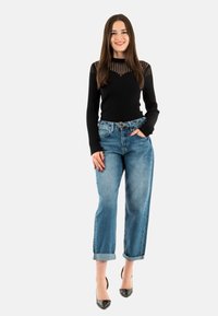 Top a maniche lunghe a coste nere con dettagli trasparenti a righe, abbinato a jeans azzurri a vita alta con risvolti e décolleté neri a punta.
