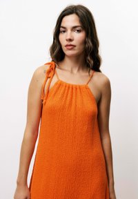 Orangenes Kleid aus strukturiertem Stoff, mit Halterneck und verstellbaren Trägern. Fällt locker mit einer entspannten Passform. Keine Muster oder sichtbare Beschläge.