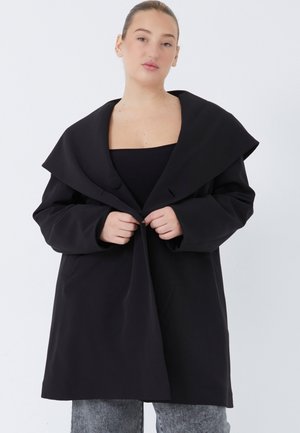 Manteau noir oversize avec un large col, fermeture à un bouton et manches longues. Fabriqué en tissu lisse et structuré.
