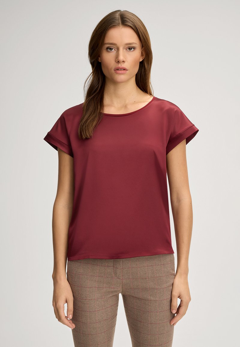 Bordeauxfarbiges kurzärmeliges Oberteil mit rundem Ausschnitt und glatter Textur, kombiniert mit karierten braunen Hosen mit roten Akzenten.