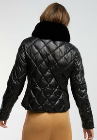 Svart vadderad jacka med krage av konstpäls, figursydd passform och jämn textur. Ryggdelen har diamantstickning och en skräddarsydd design.