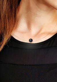 Collier pendentif clair avec une seule perle sphérique noire sur un cordon en nylon transparent fin, reposant sur un cou nu au-dessus d'un haut noir.