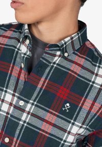 Camisa de cuadro con botones, que presenta patrones en cuadros azules, rojos y blancos, con un logo bordado en blanco en el lado izquierdo del pecho y collar puntiagudo.