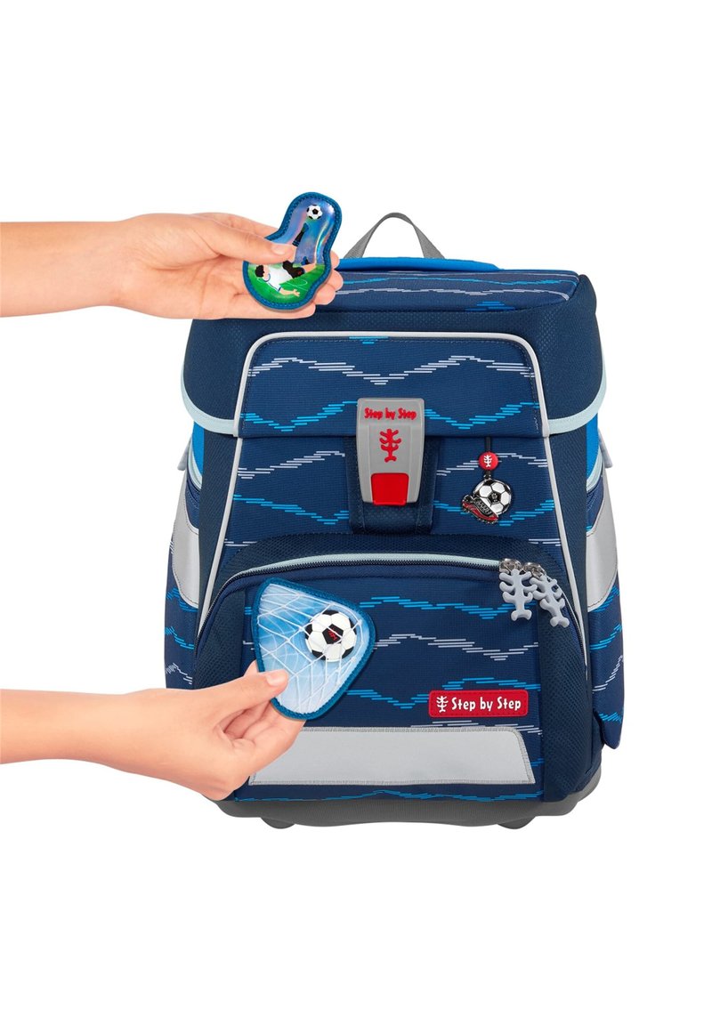 Marineblaue Tasche mit Wellenmuster, ausgestattet mit anpassbaren Patches, rotem Logo und grauen Akzenten. Hand, die einen Patch auf die Tasche platziert.
