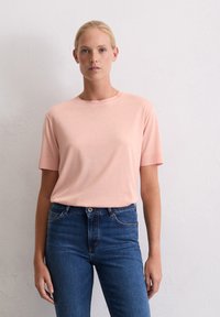 T-shirt rose clair à manches courtes avec un col rond, en tissu doux, associé à un jean en denim bleu foncé. Design simple et classique.