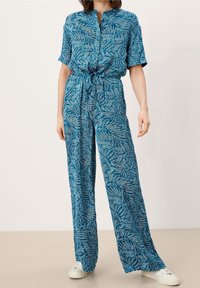 Combinaison bleu à motifs avec manches courtes, ceinture à nouer à la taille et jambes larges. Confectionnée en tissu léger avec un motif de feuilles. Dotée d'un col.