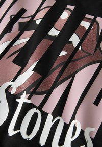 Sort t-skjorte i stoff med en grafikk av rosa lepper med glitterfinish, omgitt av fete svarte striper og hvit tekst som sier «stones».