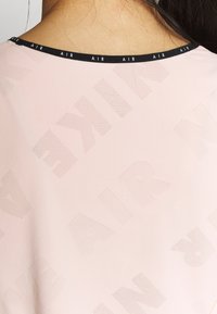 Light pink athletic shirt with a round black neckline. Subtle perforated texture featuring repeated “AIR” pattern. Smooth fabric.