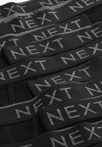 Schwarze Stoffbänder mit dem Wort "NEXT" in silberner Schrift, die eine glatte Textur und ein flaches Design aufweisen, angeordnet in überlappenden Schichten.